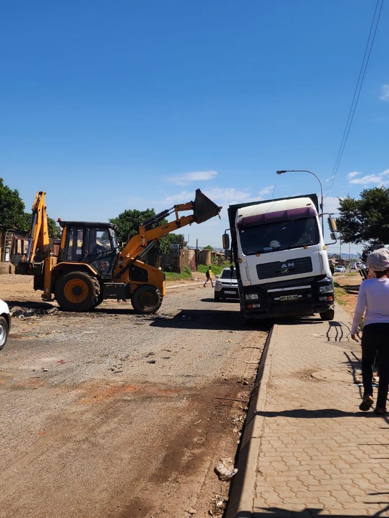 Tractor loader backhoe clearing road debris beside a commercial freight truck